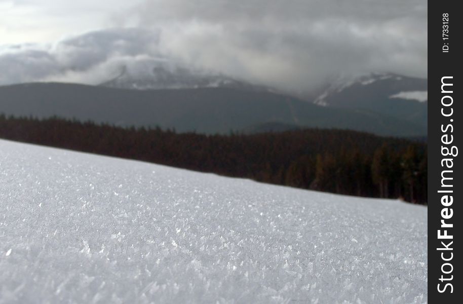 Snow-covered surface of the mountainside (and not in focus mountain and clouds behind). Snow-covered surface of the mountainside (and not in focus mountain and clouds behind)