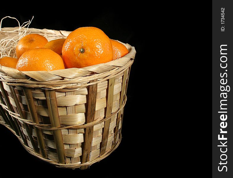 Clementines imported from Spain in a basket on a black background.  These are also knows as Satsumas and are grown in southern Louisiana.