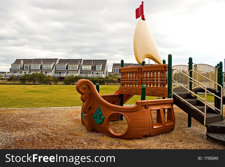 A big, plastic pirate ship makes up part of a outdoor playground for children to climb on and play with.