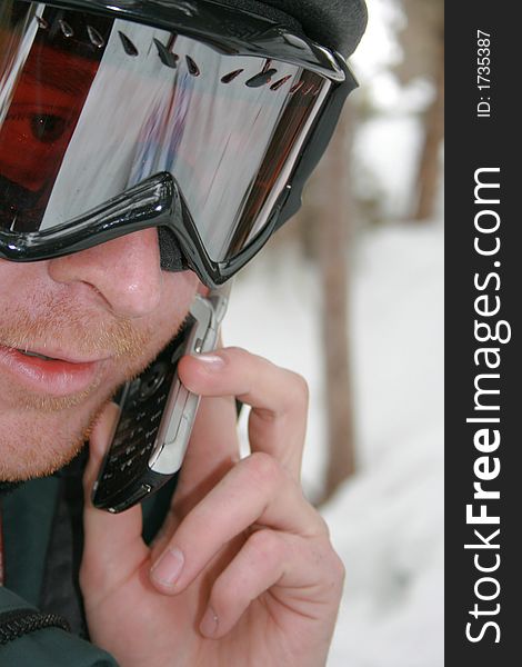 A man uses his cell phone while enjoying the outdoors skiing . A man uses his cell phone while enjoying the outdoors skiing