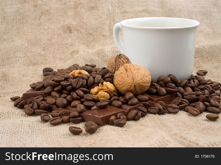 Cup of coffee, walnuts, coffee beans and bar of chocolate over linen canvas. Cup of coffee, walnuts, coffee beans and bar of chocolate over linen canvas