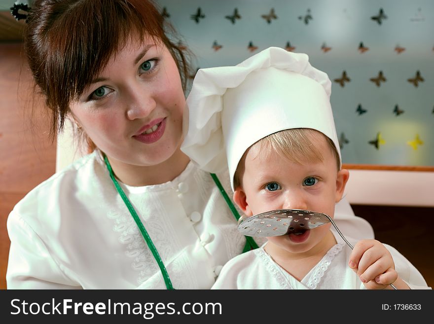 Laughing mother and her little son in cook costume at the kitchen. Laughing mother and her little son in cook costume at the kitchen