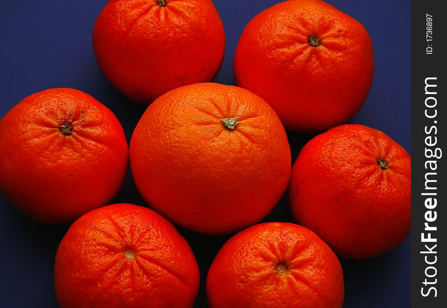 Closeup of six tangerines with one orange in the center on a blue background. Closeup of six tangerines with one orange in the center on a blue background.