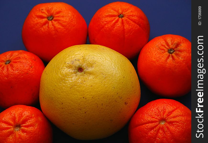 Six tangerines with one grapefruiit on a blue background with lighting effects. Six tangerines with one grapefruiit on a blue background with lighting effects.