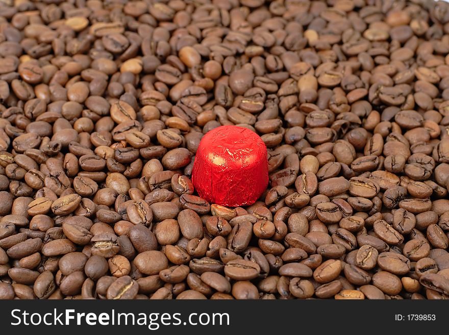 A piece of red chocolate on a heap of coffee beans . A piece of red chocolate on a heap of coffee beans