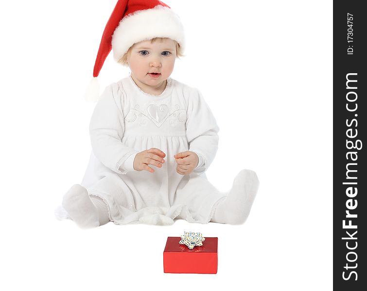 Playful baby girl in Santa's hat looking at gift in wonder. Playful baby girl in Santa's hat looking at gift in wonder