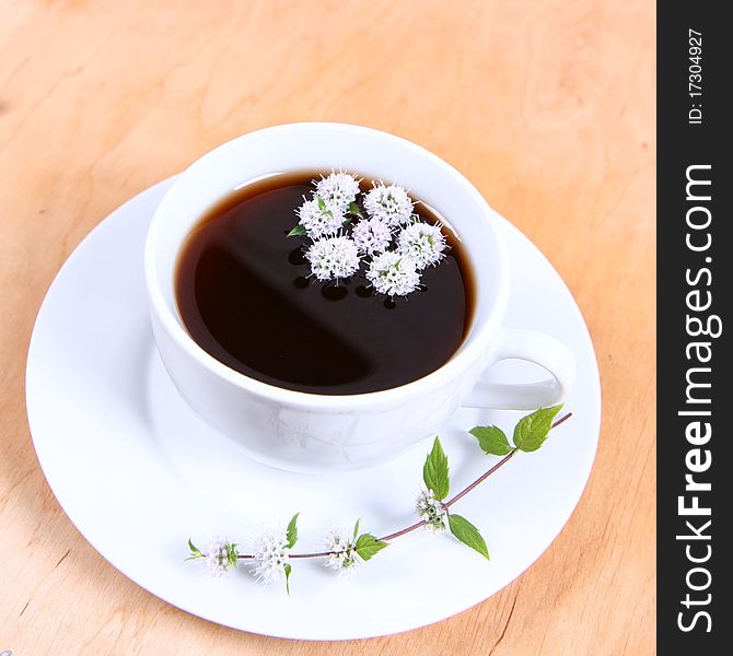 Cup of tea with flowers of peppermint floating in it on wooden background