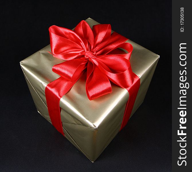 Gift in golden wrapping with red bow on black background