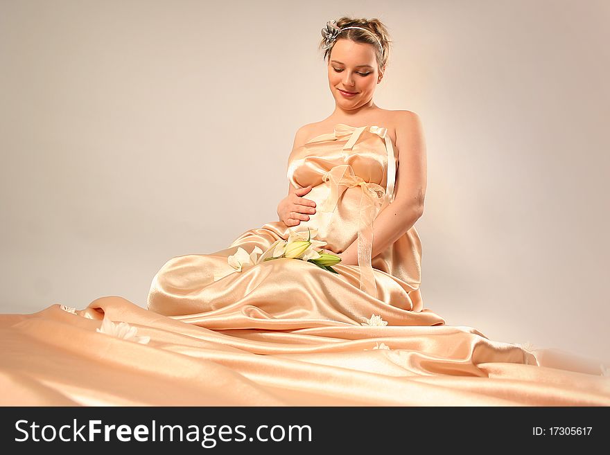 Beautiful pregnant woman wrapped in golden silk. Beautiful pregnant woman wrapped in golden silk