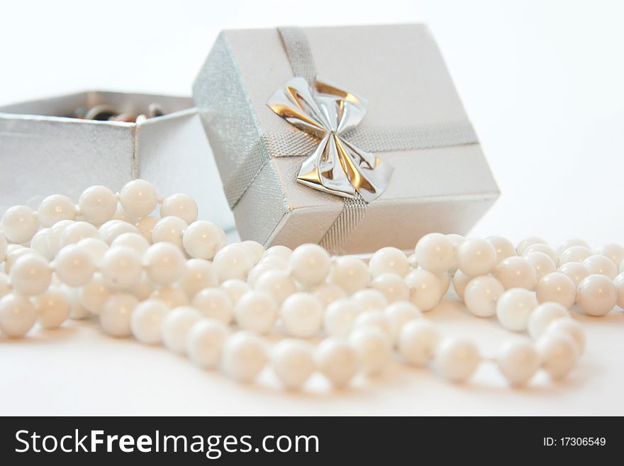 Silver gift box with a bow and white beads in the foreground. Silver gift box with a bow and white beads in the foreground