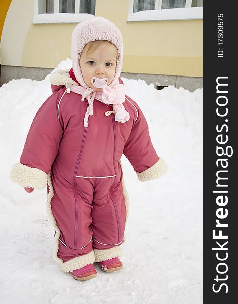 The small warmly dressed child costs in the middle of snowdrifts near a building. The small warmly dressed child costs in the middle of snowdrifts near a building