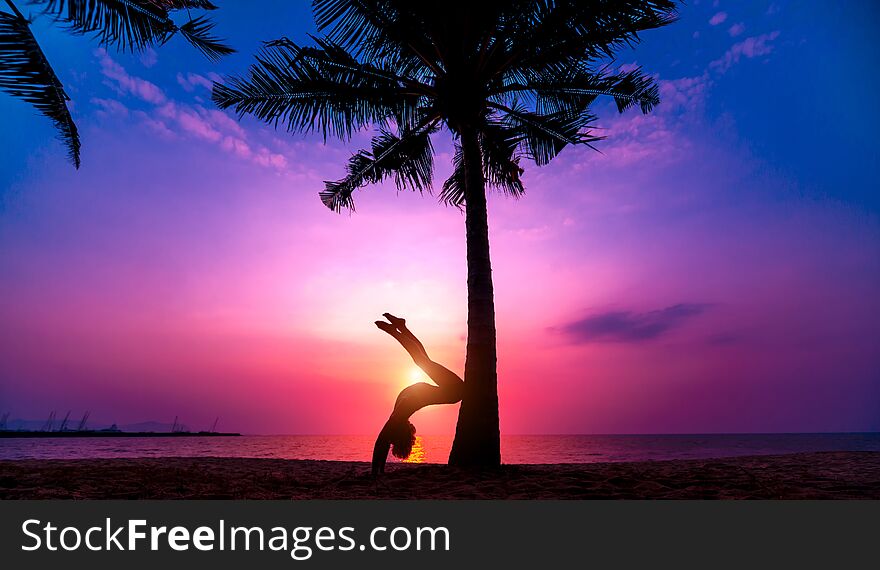 Beautiful young woman practic yoga at the beach. Early morning exercise. Sunrise. Palms background