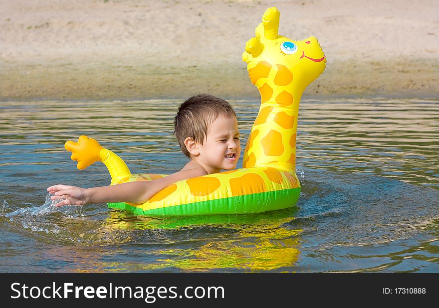 The child learns to swim in the river by means of a rubber ring. The child learns to swim in the river by means of a rubber ring