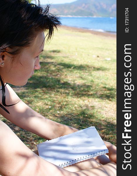 Young woman with notepad sitting on the beach