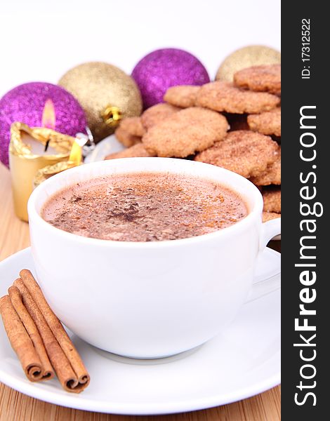 Cup of hot chocolate with cinnamon, cinnamon cookies and gold candles with christmas balls in the background. Cup of hot chocolate with cinnamon, cinnamon cookies and gold candles with christmas balls in the background