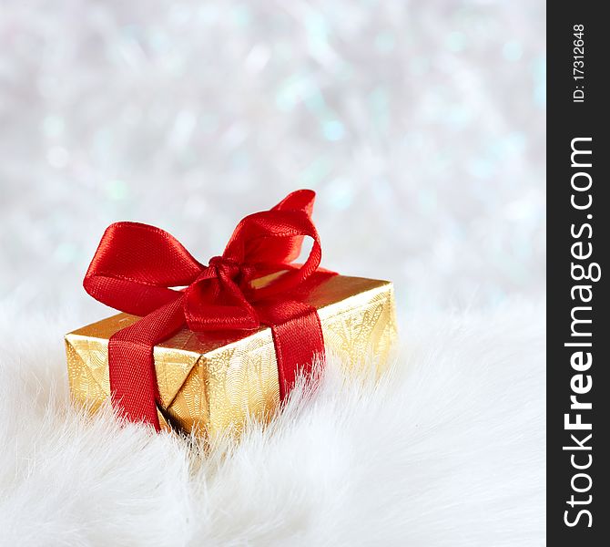 Golden Gift Box On White Fur Against Silver Blur