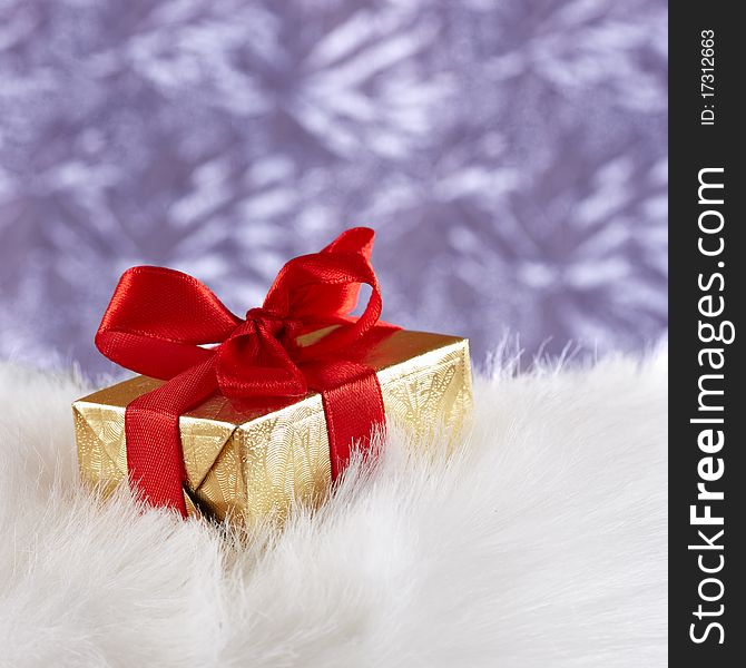 Golden gift box on white fur against blue blurre