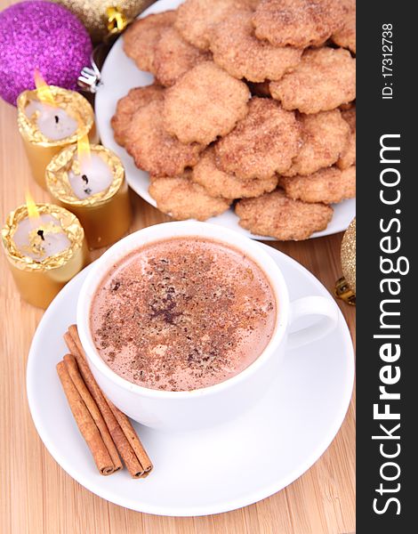 Cup of hot chocolate with cinnamon, cinnamon cookies and gold candles with christmas balls in the background. Cup of hot chocolate with cinnamon, cinnamon cookies and gold candles with christmas balls in the background