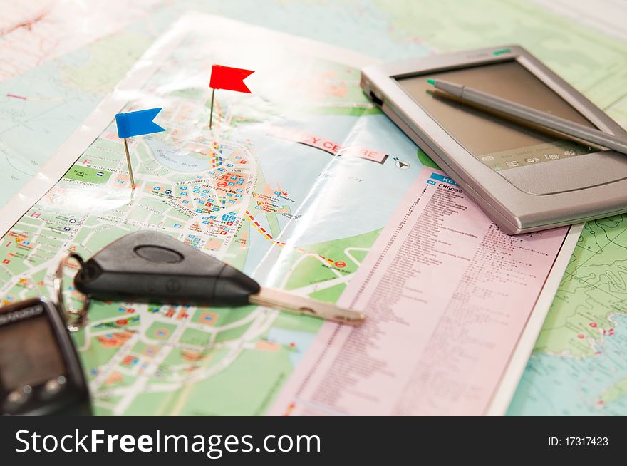 Road map with a red and blue flag, car keys, electronic organizer and credit cards. closeup. Road map with a red and blue flag, car keys, electronic organizer and credit cards. closeup.