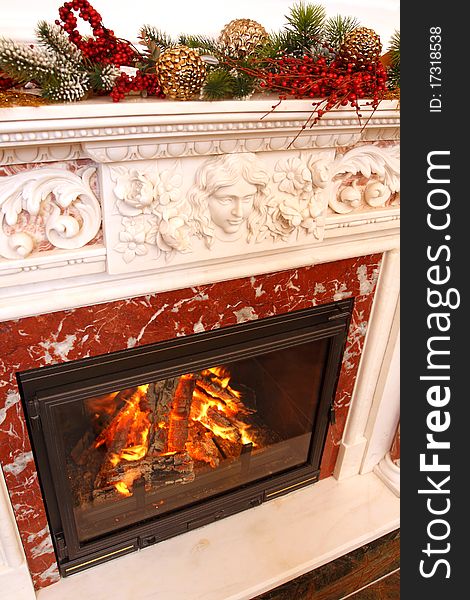 Christmas ornaments on a marble fireplace. In a fireplace fire burns.