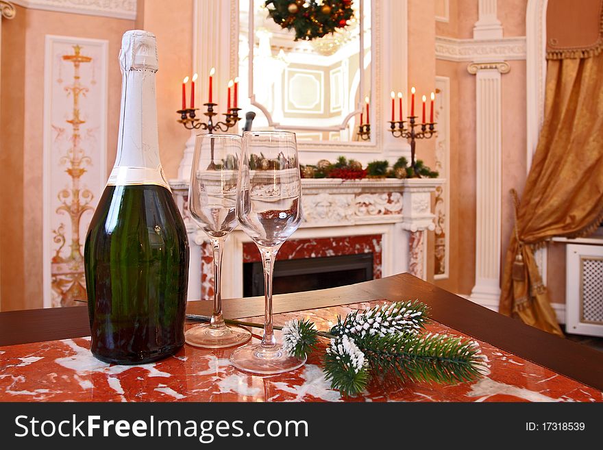 Bottle of sparkling wine and two glass glasses against a marble fireplace