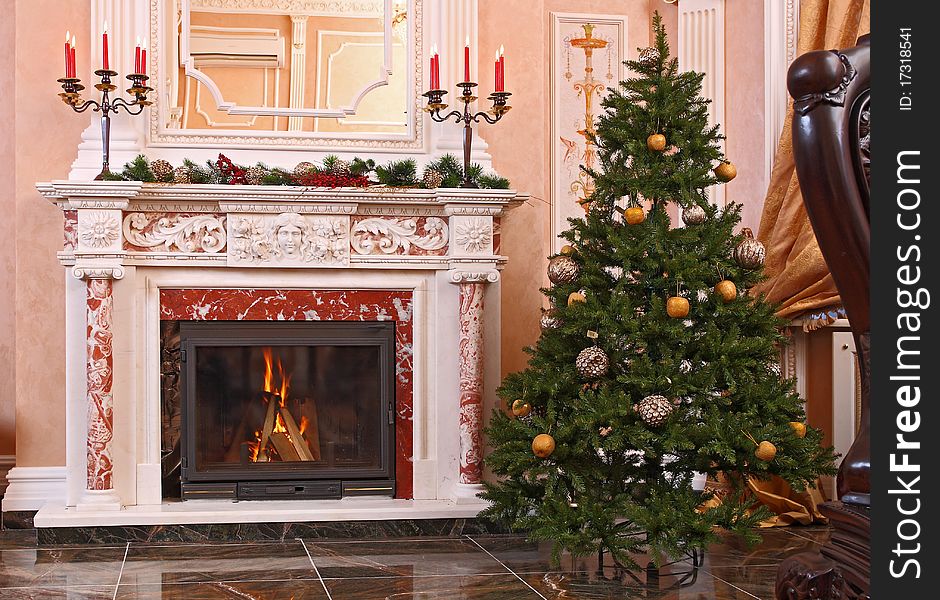 Candles in a candlestick on a fireplace in a spacious hall with a Christmas fur-tree.