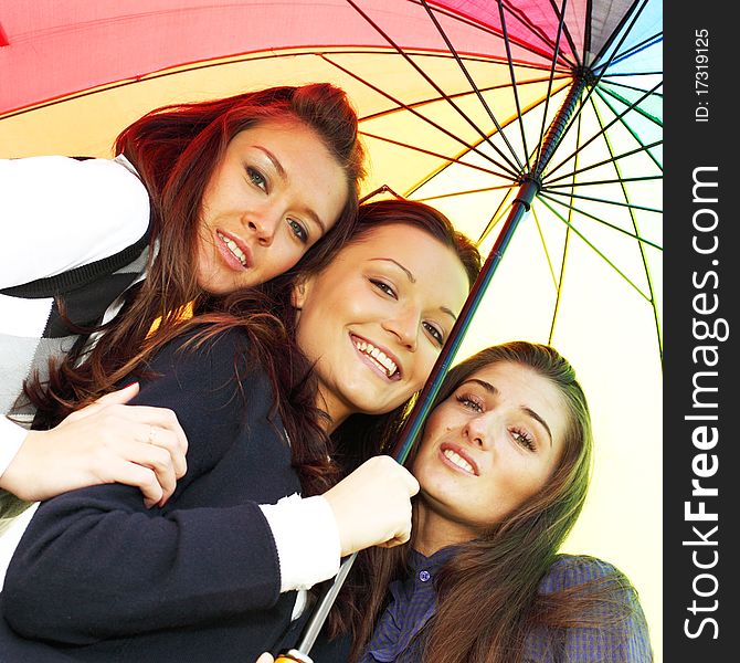 Happy smiling girlfriends stay under colourful umbrella. Happy smiling girlfriends stay under colourful umbrella