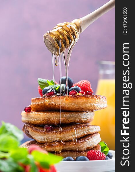 Pouring Honey on Pancakes Stack Topped with fresh Fruits. Shrove Tuesday Breakfast