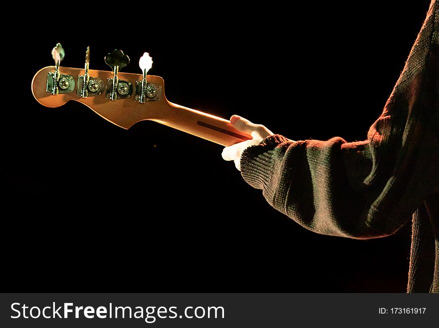 A detailed selective focus shot on the hand of a guitar player playing by night, neck, headstock and tuning pegs  against a black background. A detailed selective focus shot on the hand of a guitar player playing by night, neck, headstock and tuning pegs  against a black background