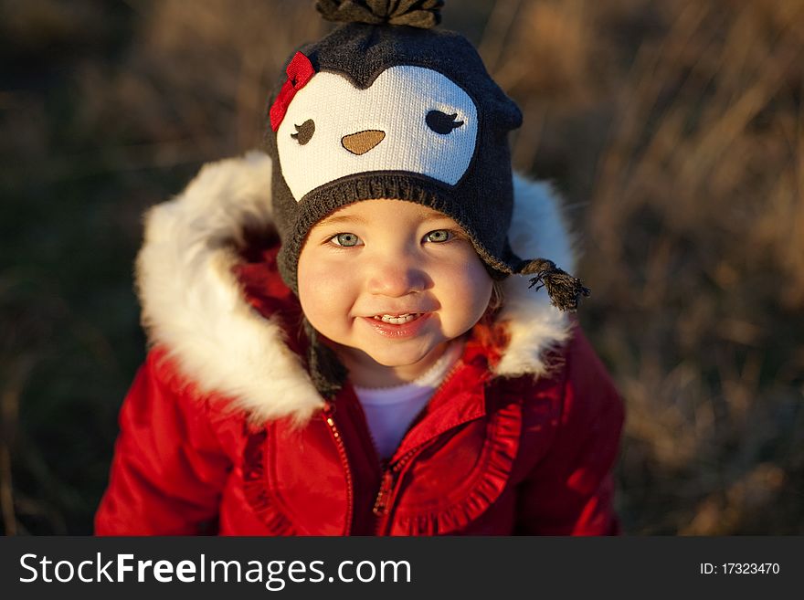 A cute girl or toddler in a red winter jacket with white trim smiles at the camera in her penguin winter hat. A cute girl or toddler in a red winter jacket with white trim smiles at the camera in her penguin winter hat