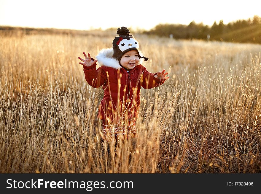 A cute girl toddler running through a field at sunset laughing and having a great time in her red winter coat and adorable penguin hat. A cute girl toddler running through a field at sunset laughing and having a great time in her red winter coat and adorable penguin hat.