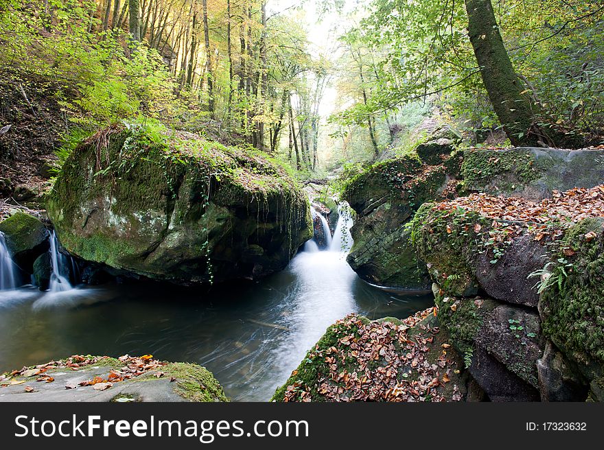 Autumn forest waterfall running through the mossy rocks