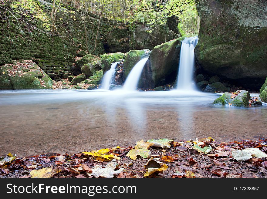 Autumn forest waterfall falling from the mossy rocks