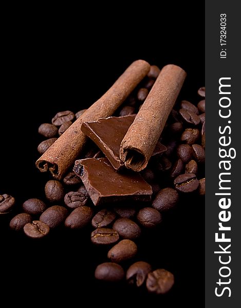 Cinnamon sticks over coffee beans and chocolate on black