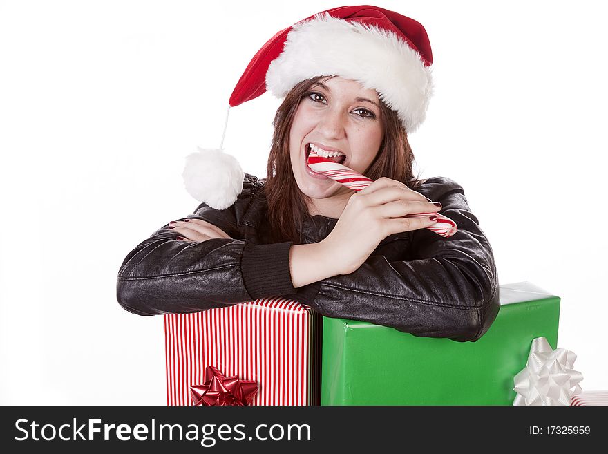 A woman with a Santa hat is leaning on some presents eating a peppermint stick. A woman with a Santa hat is leaning on some presents eating a peppermint stick.