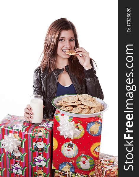 A woman is by a stack of presents with a glass of milk eating a cookie. A woman is by a stack of presents with a glass of milk eating a cookie.