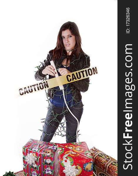 A woman is plugging in Christmas lights by a stack of presents. The lights are tangled around her and a caution sign crosses her body. A woman is plugging in Christmas lights by a stack of presents. The lights are tangled around her and a caution sign crosses her body.