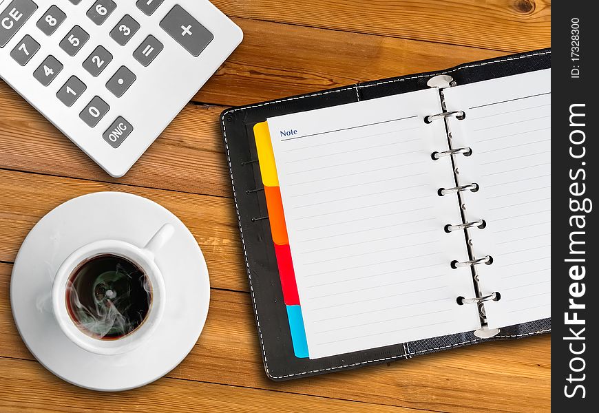 White calculator and white notebook and white cup of hot coffee on wood table