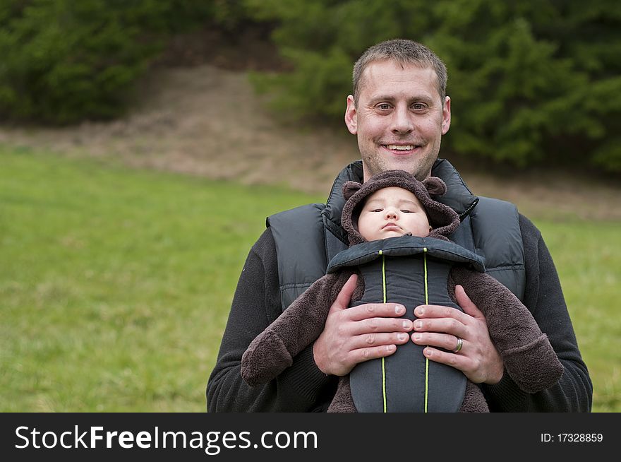 Father with a front baby carrier, holding his newborn son in a cute little pouch in front of his chest. Father with a front baby carrier, holding his newborn son in a cute little pouch in front of his chest