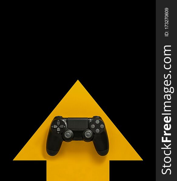 Modern black gamepad on a yellow arrow on a black background. Joystick on a yellow direction indicator on a dark background. Flat