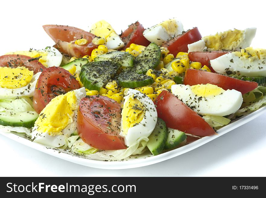 Plate of vegetable salad with eggs, sliced tomatoes, cucumber, lettuce, corn, basil