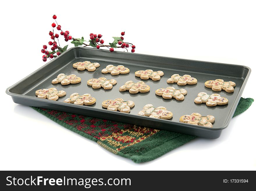 A cookie sheet containing 15 gingerbread cookies on a Christmas-colored terry towel.  Isolated on white.
