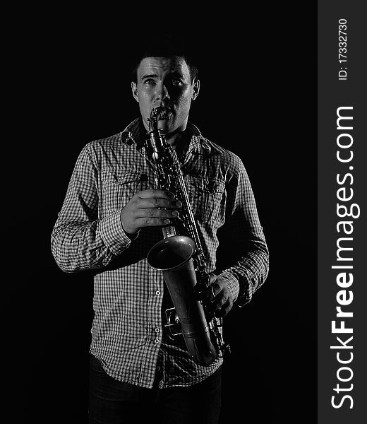 Young handsome man playing music on saxophone. black background