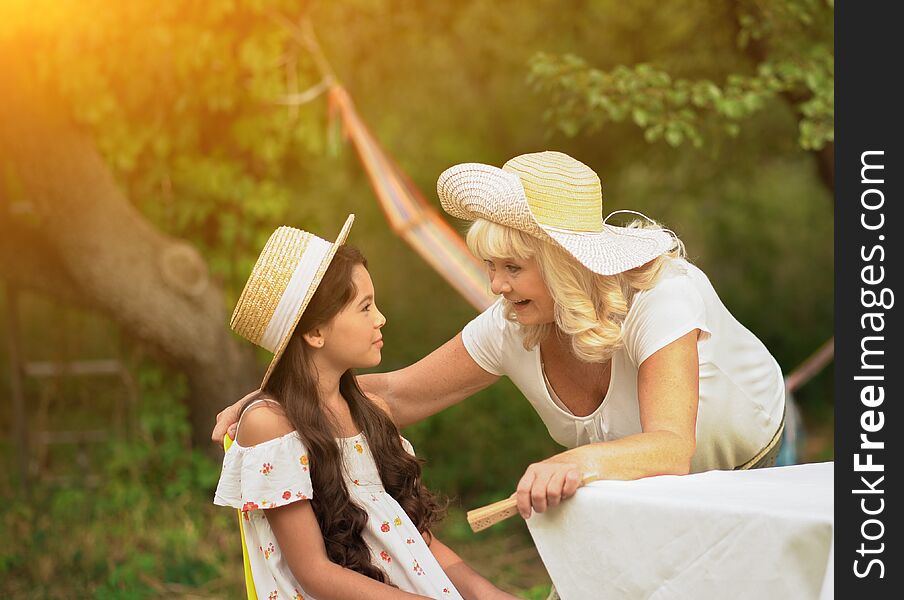 Grandmother speak to little girl sitting on chair in garden. Old lady has conversation with granddaughter outdoor across park. Grandmother speak to little girl sitting on chair in garden. Old lady has conversation with granddaughter outdoor across park.