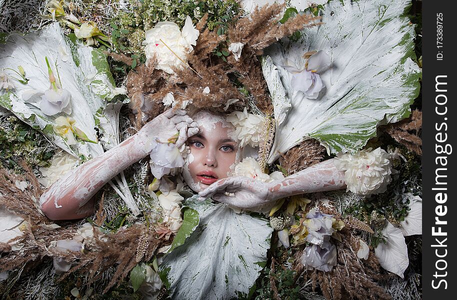 Female portrait in fairy tale stylisation surrounded with natural plants and flowers.