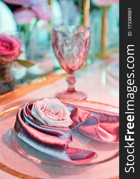 Plate with silk napkin and pink rose. Beautiful table setting with flowers decorations and glass