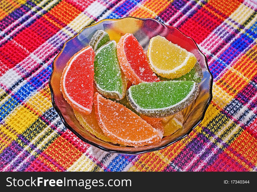 Citric segments in sugar, in saucer, on a background of a motley cloth