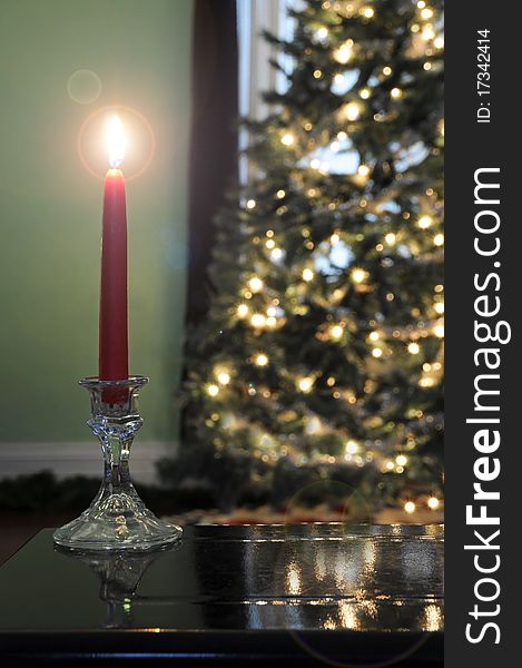 Lit candle glowing bright in front of a lit Christmas tree. Lit candle glowing bright in front of a lit Christmas tree