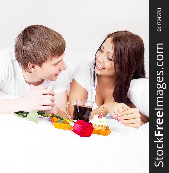 Young man bringing his woman a rose and coffee in bed. Young man bringing his woman a rose and coffee in bed
