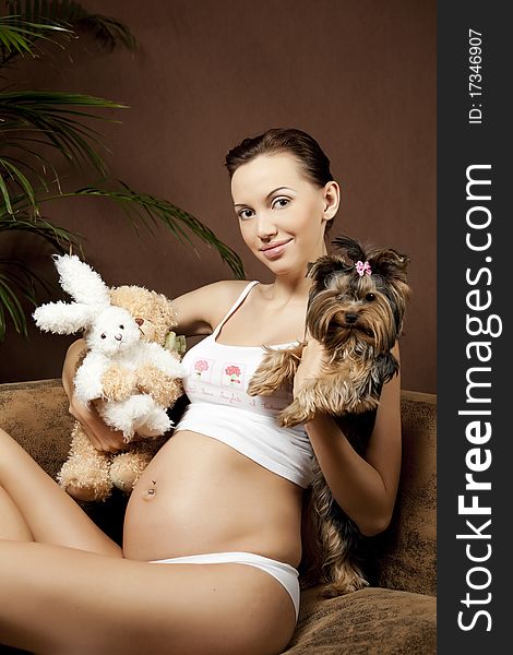 Pregnant woman, sitting on the sofa with toys and little dog and